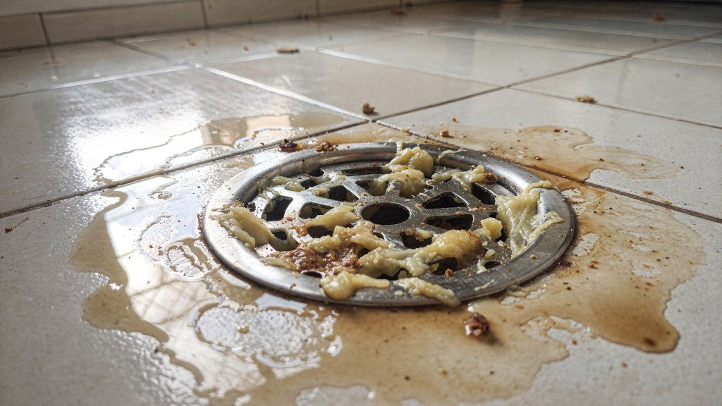 Ralo de piso de cozinha com água parada e resíduo de gordura amarelada acumulado na grelha e ao redor do ralo em piso de cerâmica